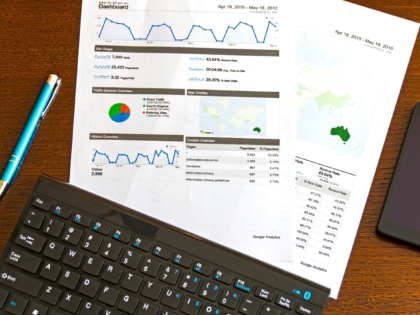 Flatlay of a business analytics report, keyboard, pen, and smartphone on a wooden desk.