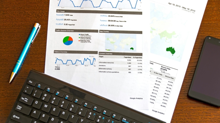 Flatlay of a business analytics report, keyboard, pen, and smartphone on a wooden desk.