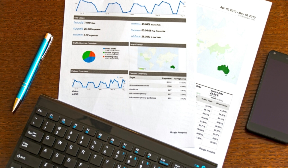 Flatlay of a business analytics report, keyboard, pen, and smartphone on a wooden desk.